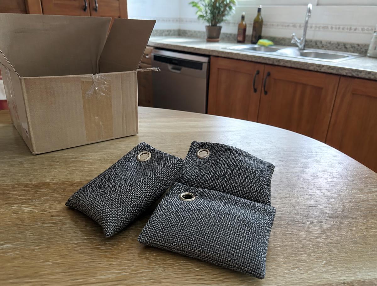 Tres bolsas purificadoras de carbón de bambú sobre la mesa de una cocina, junto a la caja de envío